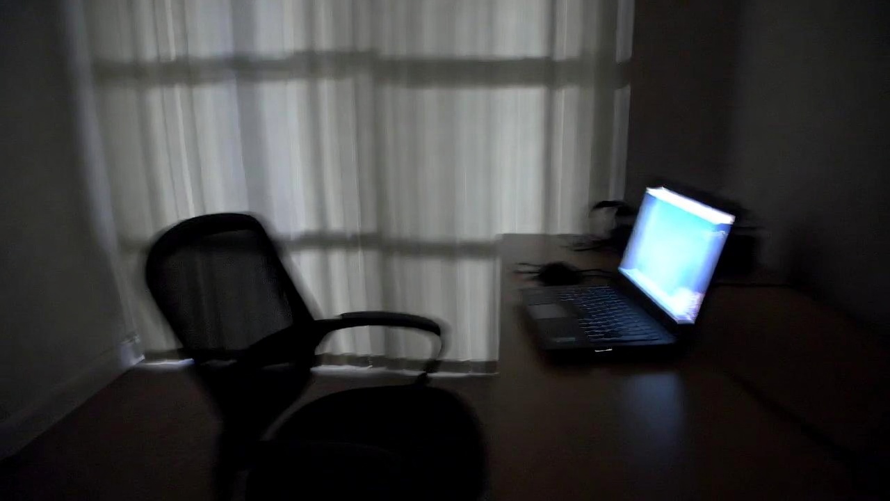 Empty chair pulled back from a desk lit by a single glowing laptop screen, generic suburban interior at night, strongly blurred.