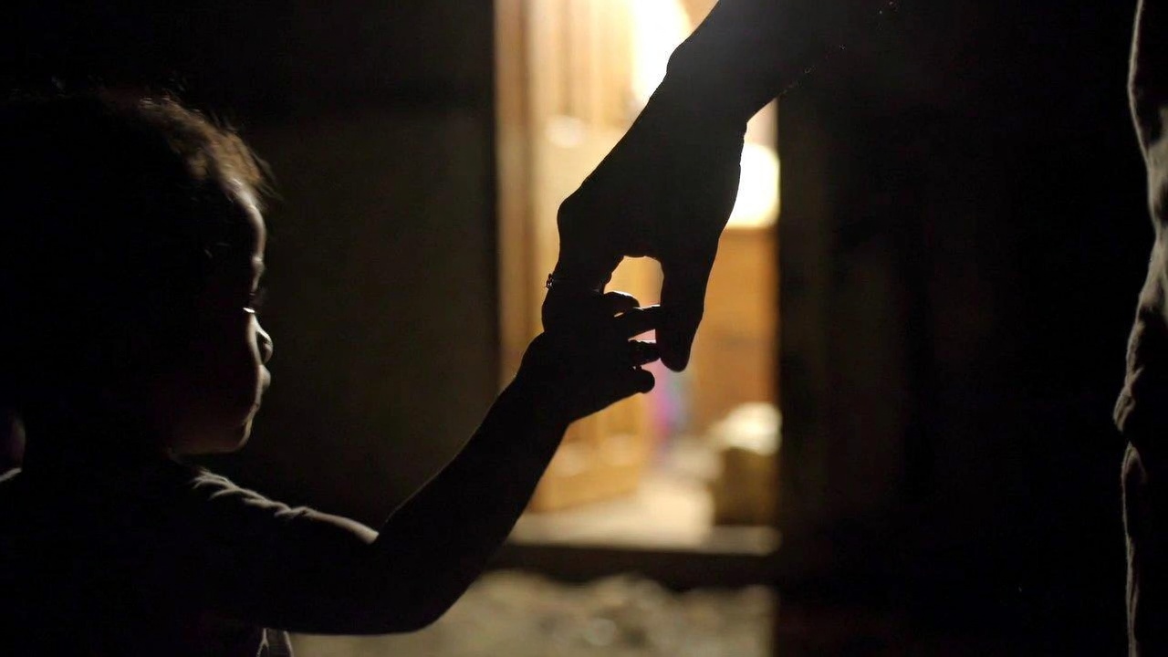 A small child's hand reaching up to grasp an adult woman's hand in a warm, lit doorway, strongly blurred.